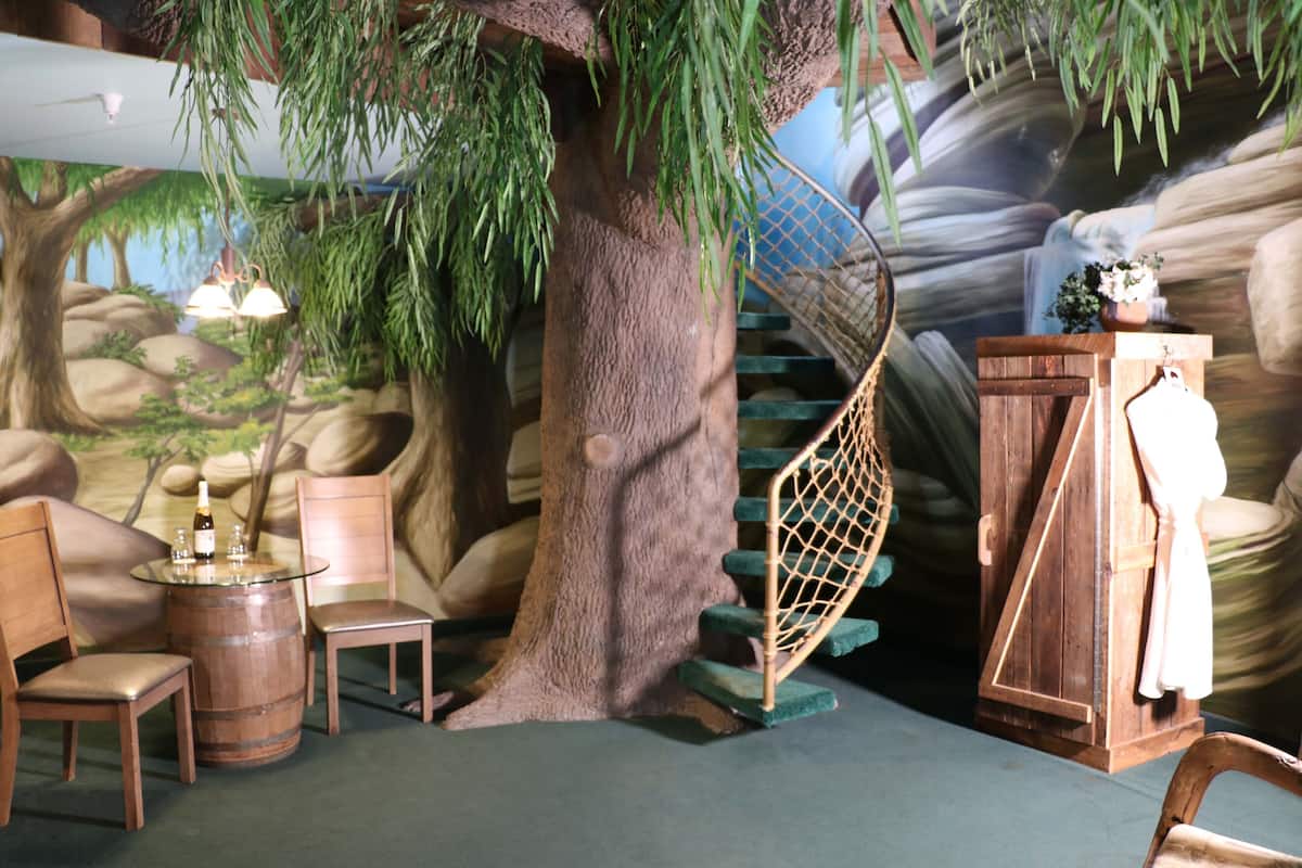 Une pièce avec un arbre, un escalier en bois et une table entourée de chaises.
