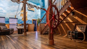 Habitación con temática náutica, suelo de madera, timón de barco y un mural del océano.