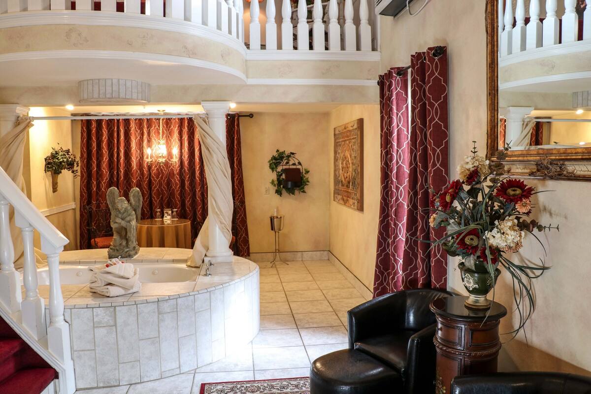 Un vaste hall d’entrée avec un escalier en marbre, un comptoir d’accueil, un fauteuil en cuir noir et un vase décoratif rempli de fleurs.
