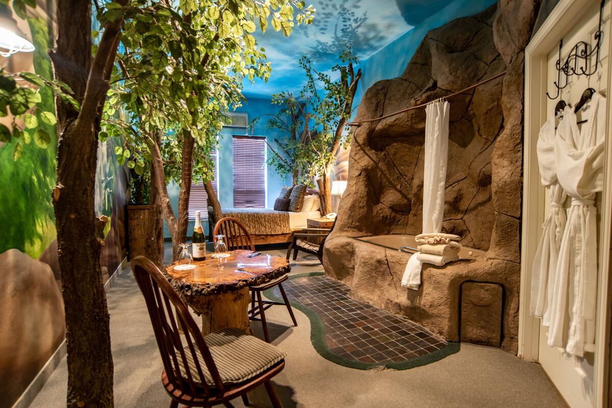 Une pièce avec un mur en pierre, une table en bois, des chaises, un banc et une baignoire.