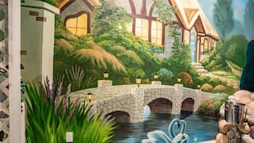 A mural of a cottage with a stone bridge over a pond, swans, and lush greenery.