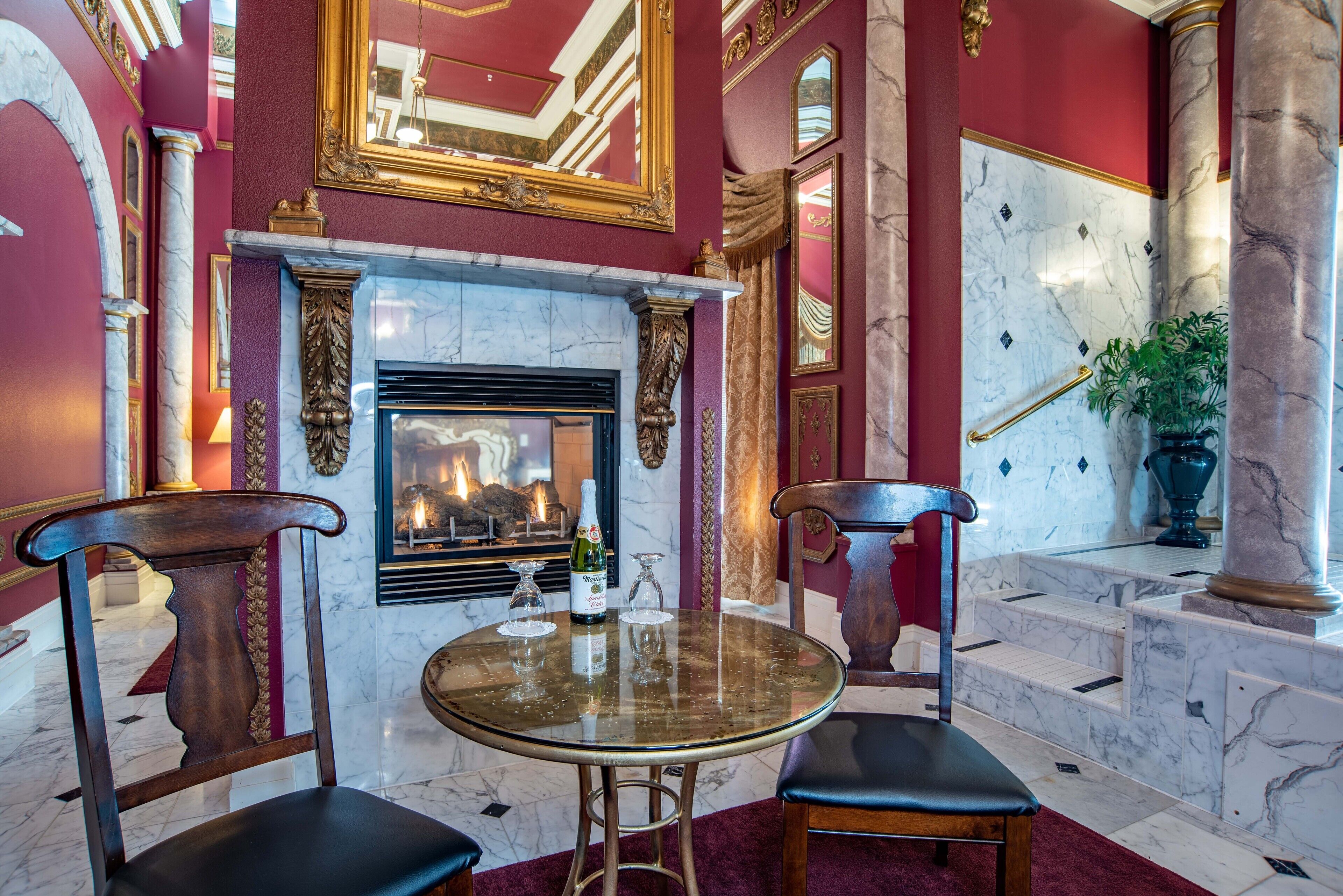 Une chambre luxueuse avec une cheminée en marbre, deux fauteuils en bois, une table en verre et un tapis rouge.