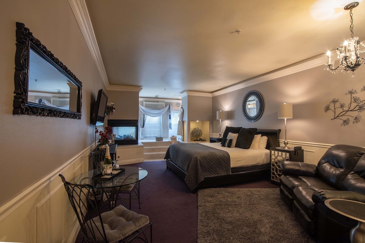 Une chambre d’hôtel avec un lit, un canapé, une table à manger avec des chaises, un lustre et un miroir au mur.