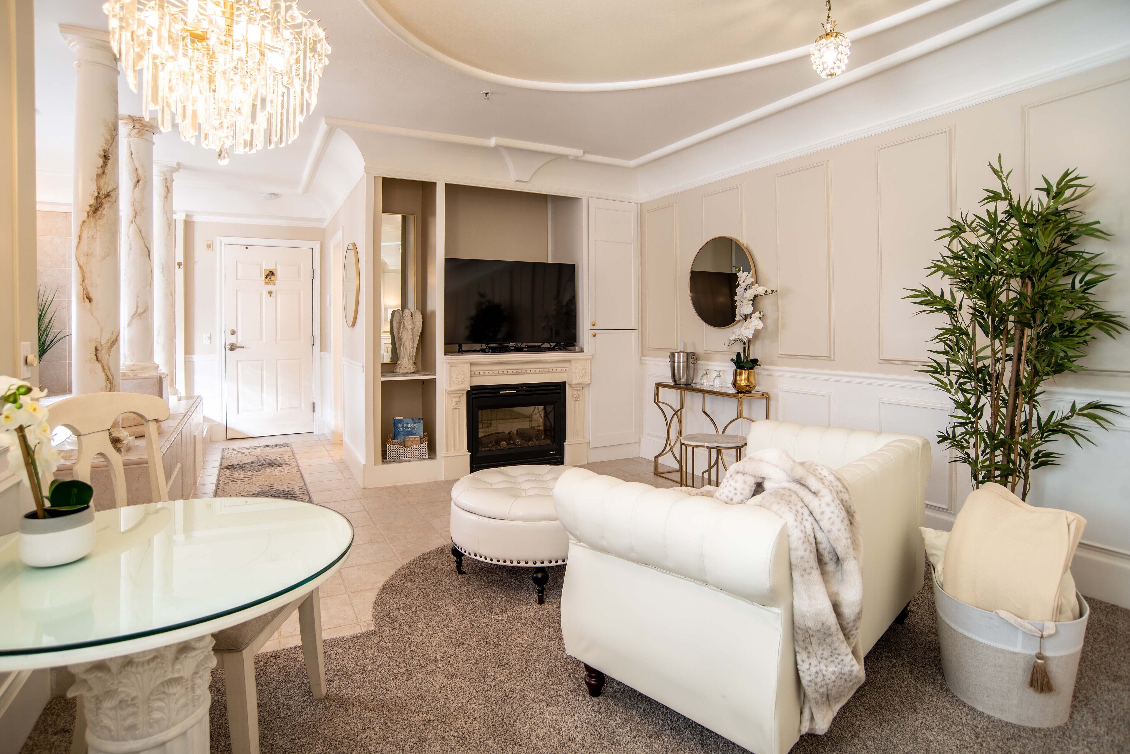 Een ruime woonkamer met een witte bank, een glazen salontafel, een open haard en een televisie.