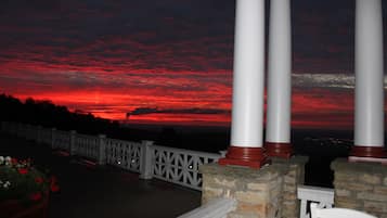 A balcony with white railings and columns, overlooking a sunset with red clouds.