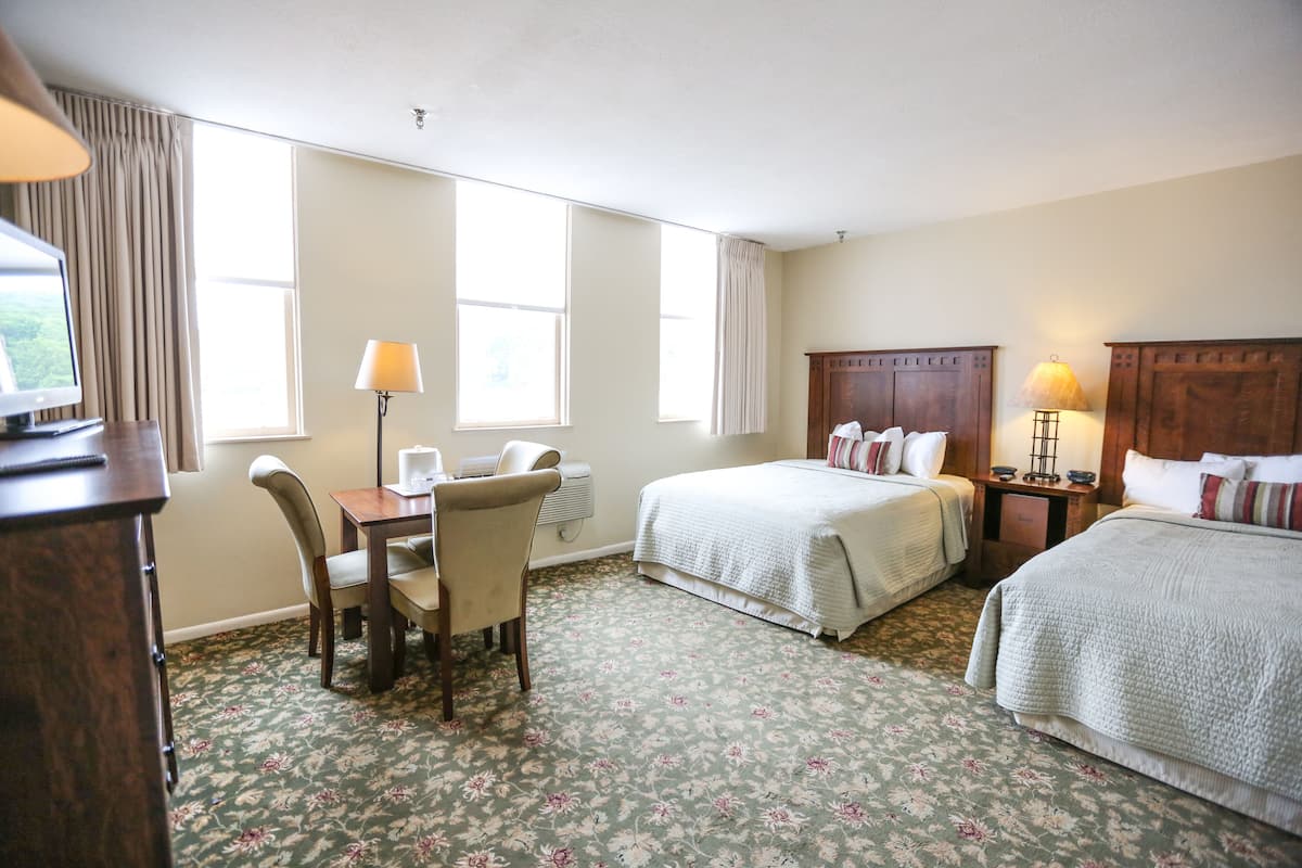 A hotel room with two beds, a desk with a chair, a television, and a window with curtains.