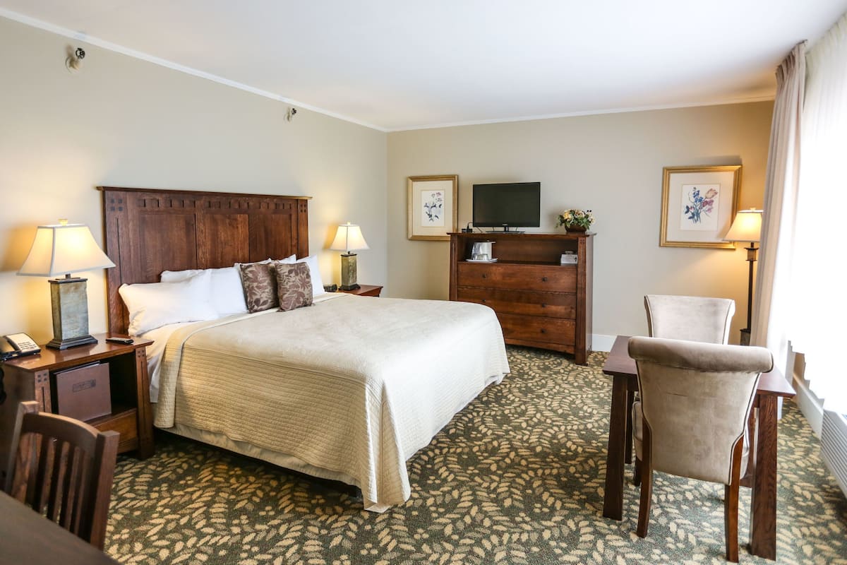 A hotel room with a large bed, a wooden dresser, a television, and a chair.