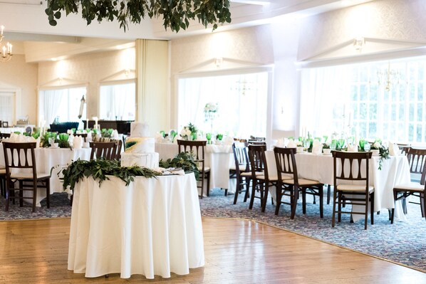 A banquet hall with round tables covered in white tablecloths, wooden chairs, and green foliage centerpieces. - The Historic Summit Inn (Hopwood)