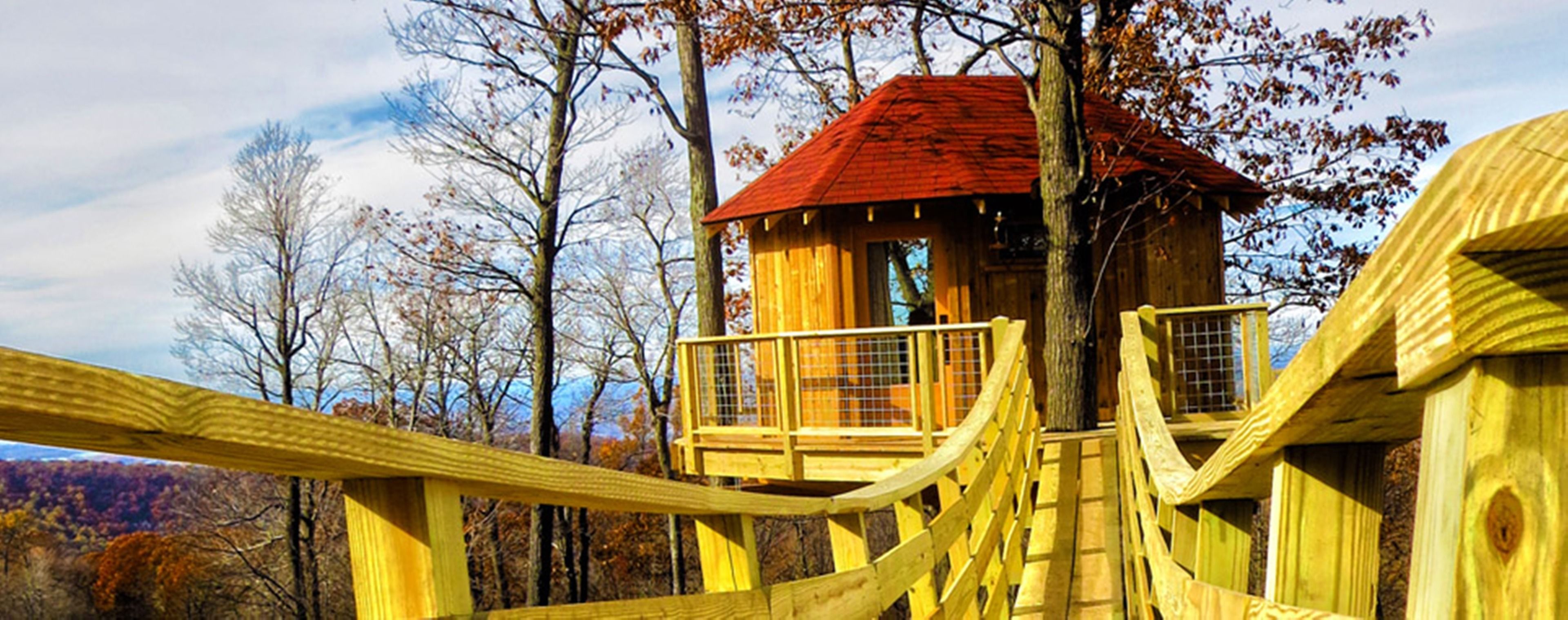 A wooden treehouse with a red roof, surrounded by trees and a wooden bridge.