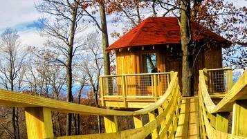 A wooden treehouse with a red roof, surrounded by trees and a wooden bridge.