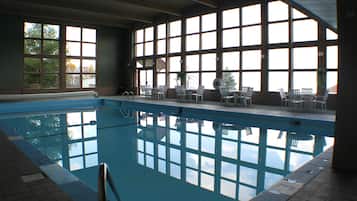 Una piscina interior con ventanales amplios, sillas y suelo de baldosas.