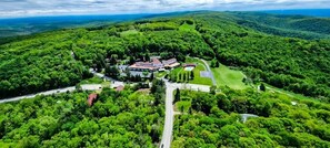 An aerial view of a resort with a central building surrounded by lush greenery, multiple access roads, and a clear sky.