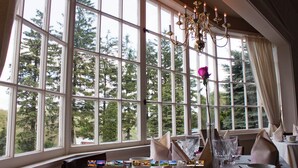 A room with large windows, a chandelier, and neatly arranged dining tables.