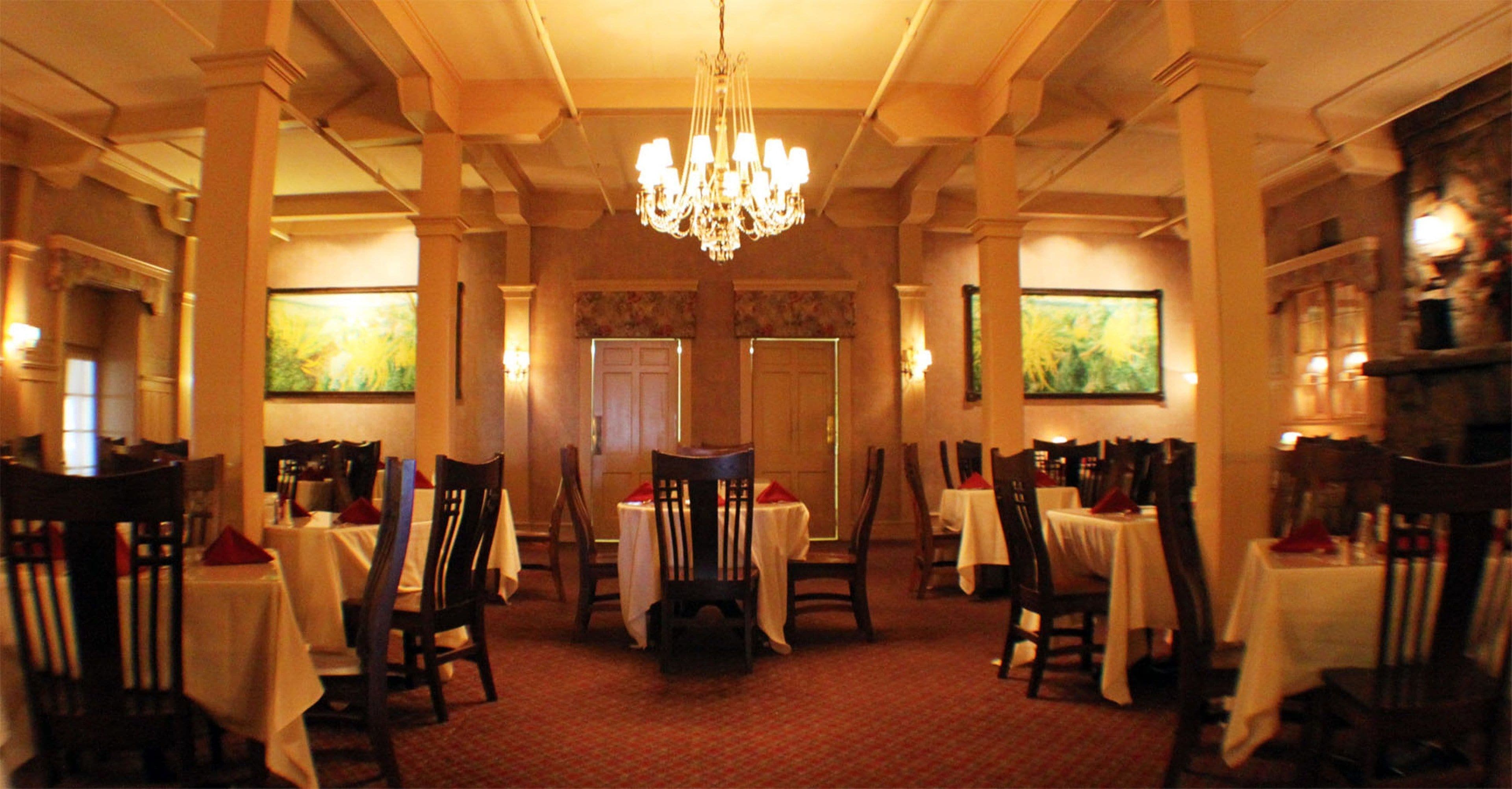 Un comedor formal con mesas dispuestas para el servicio, una araña y obras de arte enmarcadas en las paredes.