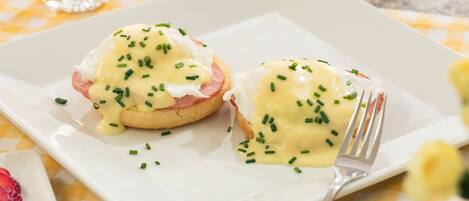 A breakfast plate with eggs benedict and a glass of orange juice on a checkered tablecloth.