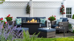 An outdoor patio with a fire feature, wicker furniture, and hanging flower baskets. - Old Harbor Inn (Chatham)
