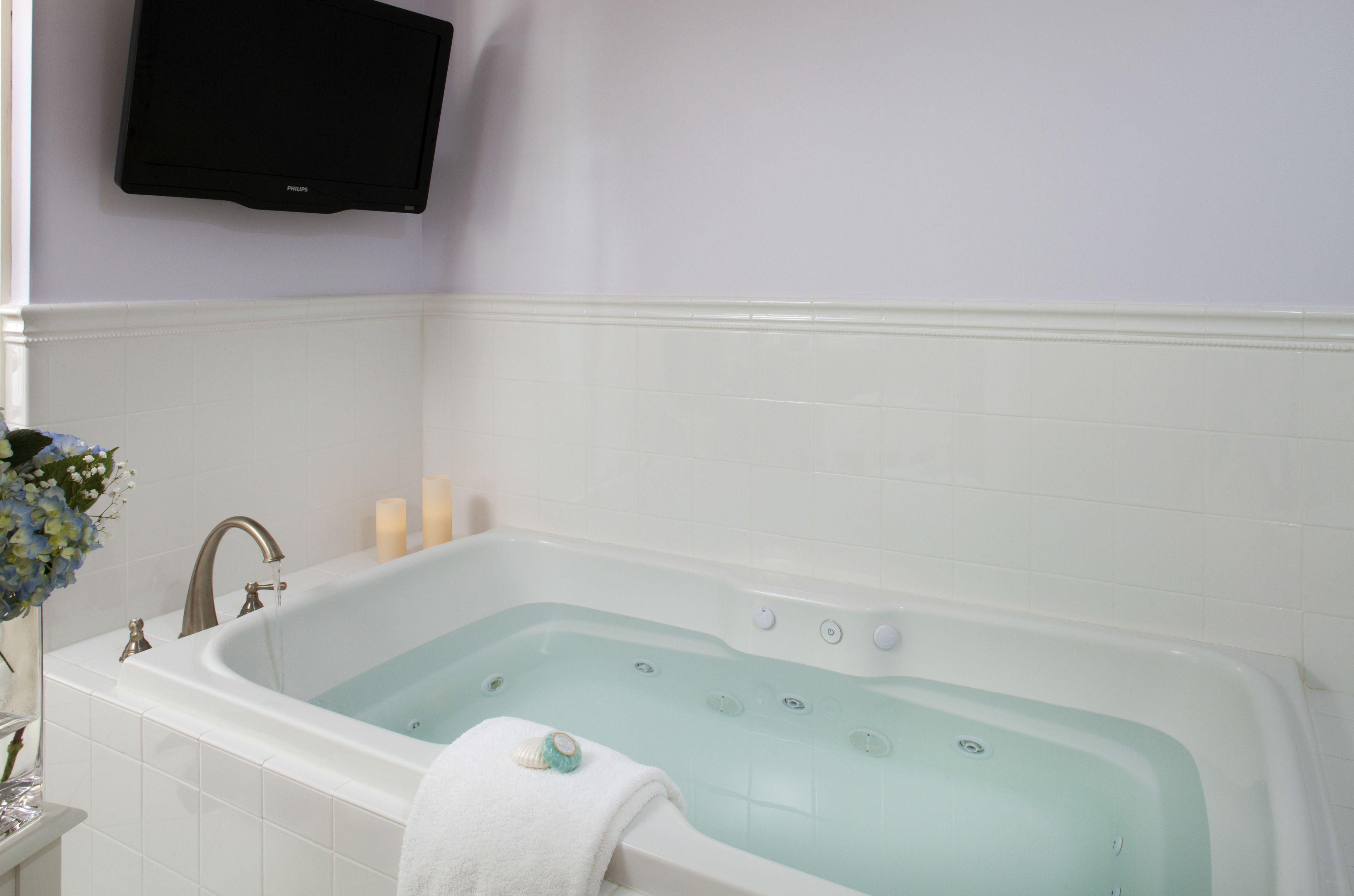 Un baño con bañera, lavamanos y televisor en la pared.