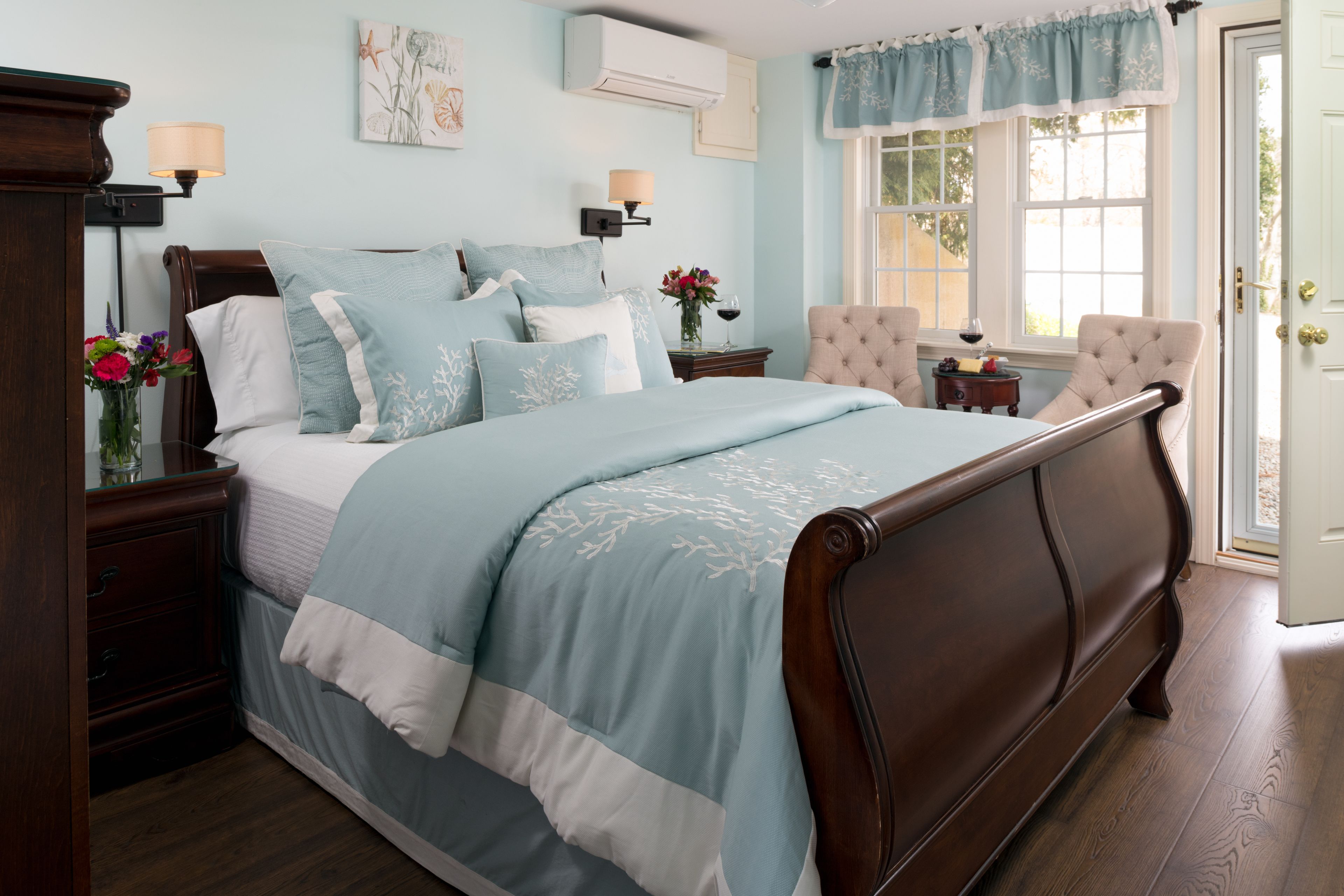 A bedroom with a large bed, a nightstand with a lamp, a chair, and a window with curtains.