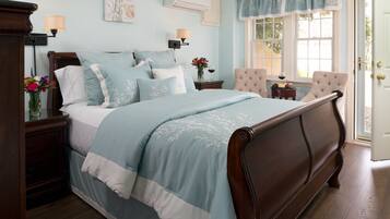 A bedroom with a large bed, a nightstand with a lamp, a chair, and a window with curtains.