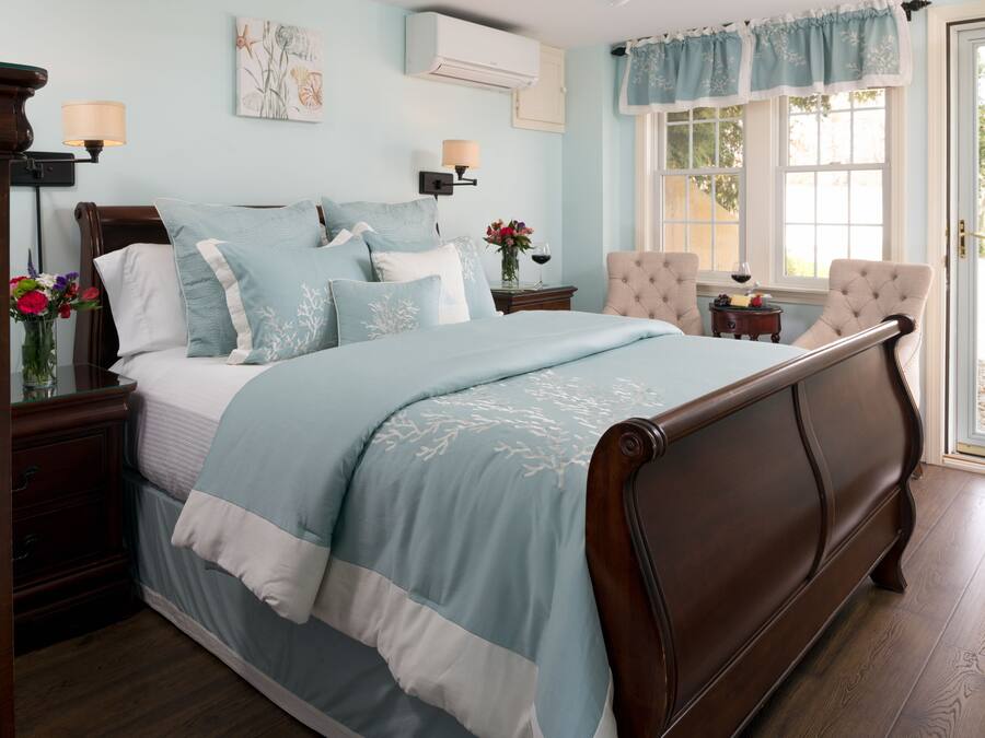 A bedroom with a large bed, a nightstand with a lamp, a chair, and a window with curtains.