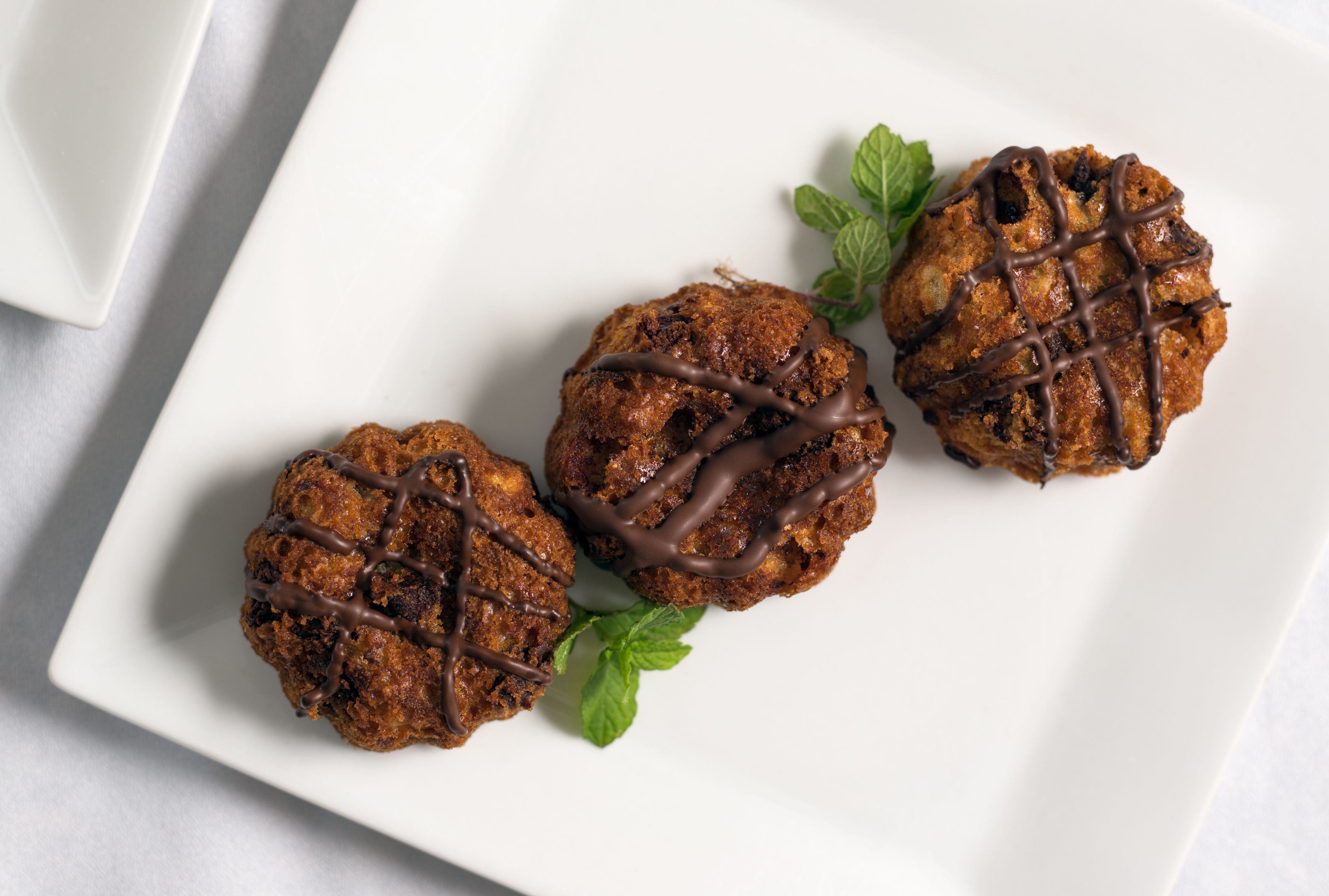 Trois biscuits au chocolat, nappés d’un filet de chocolat, présentés sur une assiette blanche et décorés de feuilles de menthe.