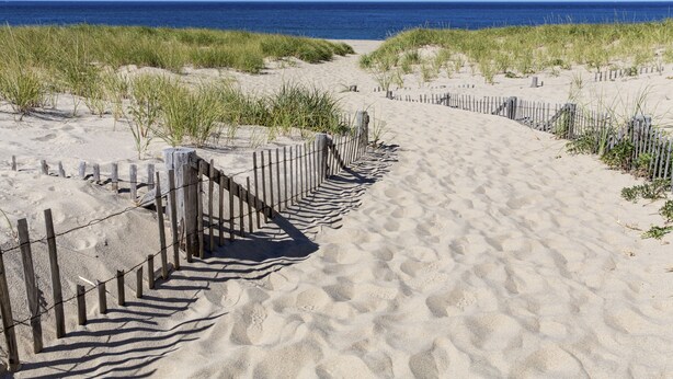 A sandy beach path with wooden fencing, leading to the ocean. - Old Harbor Inn (Chatham)