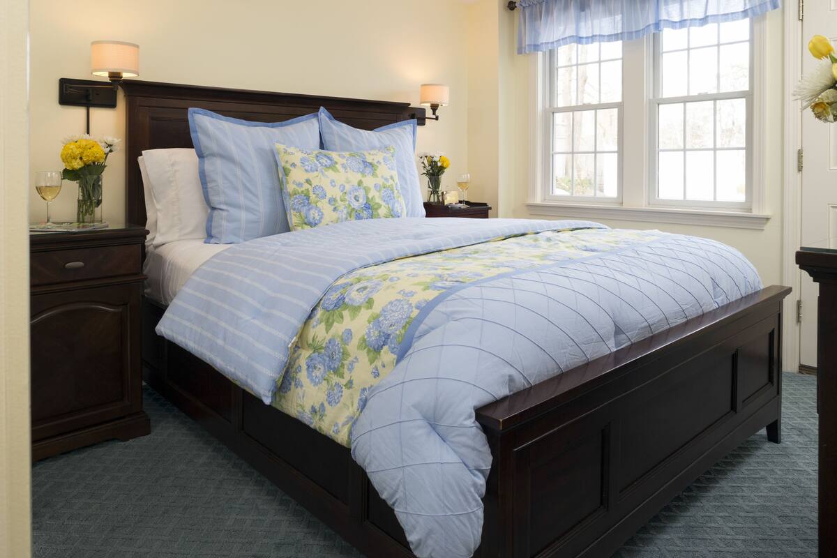 A well-lit bedroom with a large bed, a nightstand with a lamp, and a window with curtains.