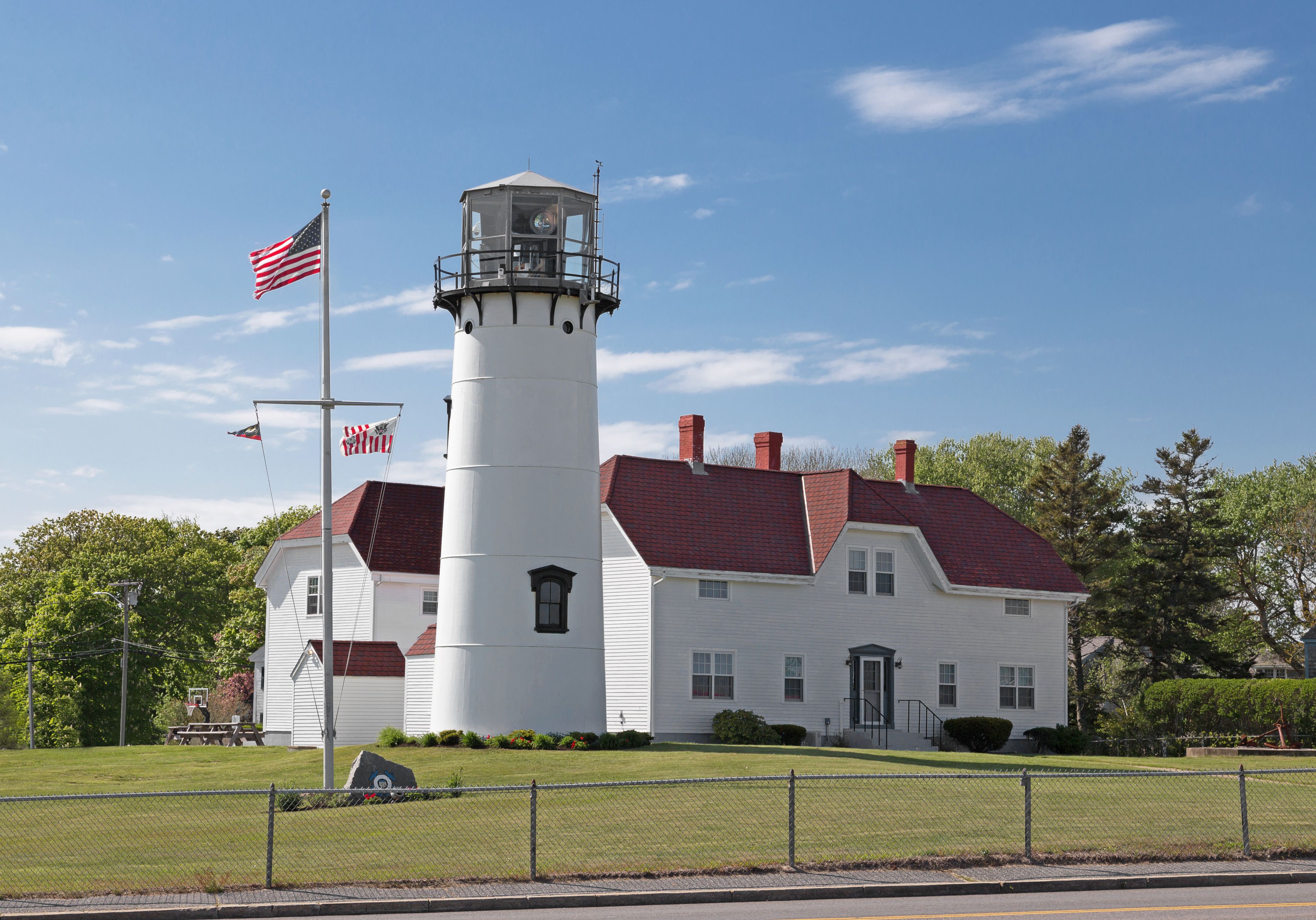 A white lighthouse with a red roof, surrounded by a well-maintained lawn and a fence.
