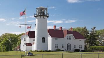 A white lighthouse with a red roof, surrounded by a well-maintained lawn and a fence.