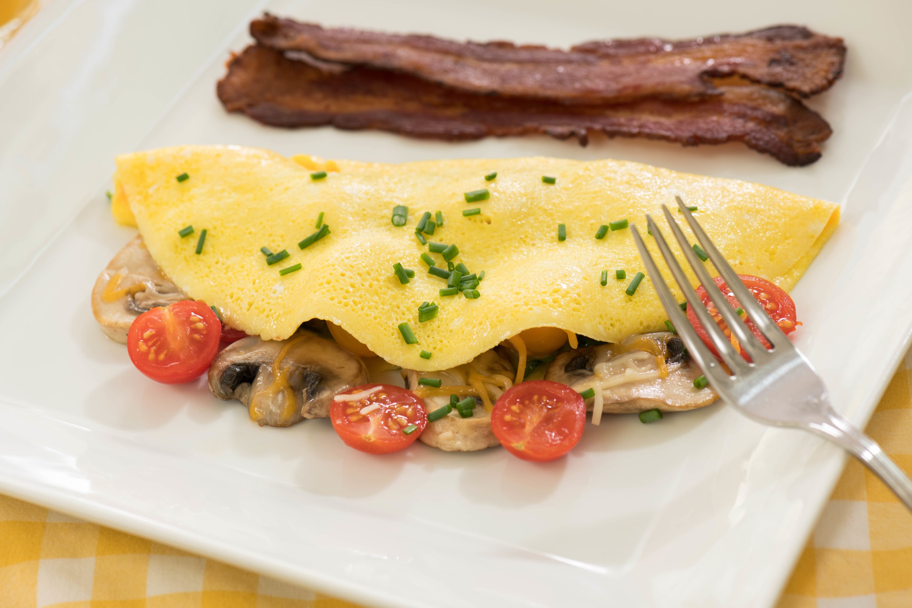 A plate with an omelette, bacon, mushrooms, and cherry tomatoes.