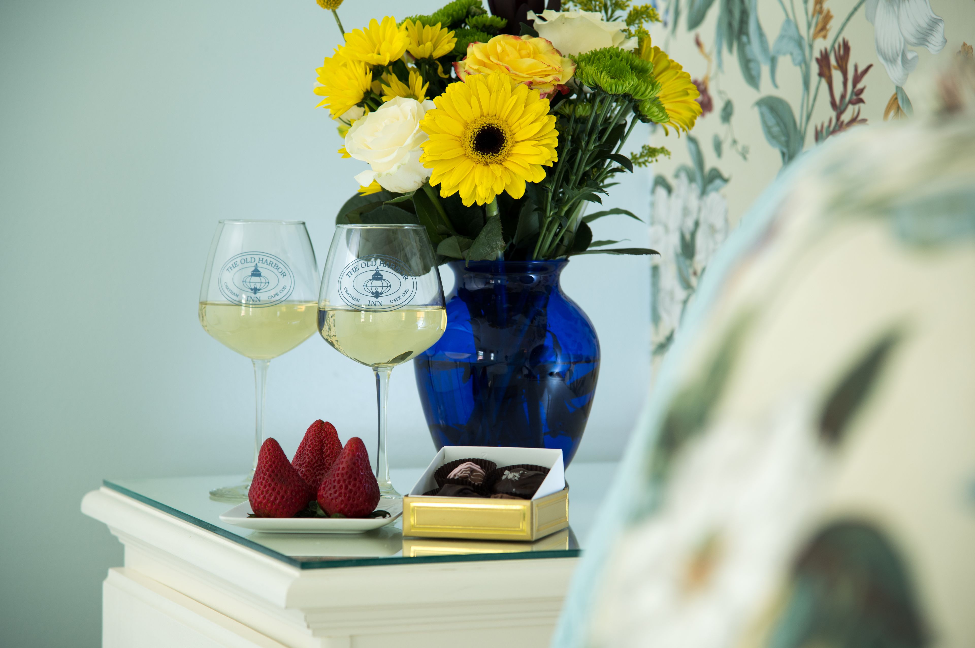 Une table avec deux verres à vin, un vase de fleurs, des fraises et des chocolats.
