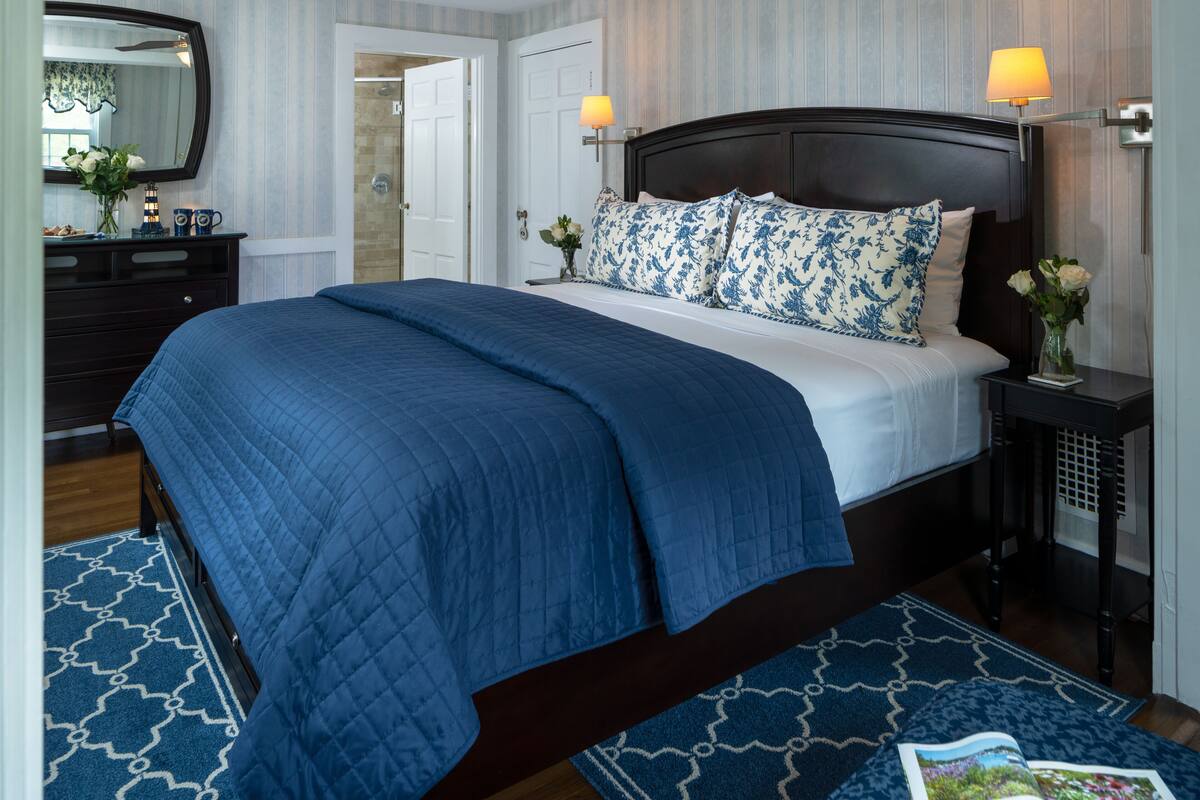 A neatly made bed with a blue quilt, a dark wooden headboard, and two bedside lamps.