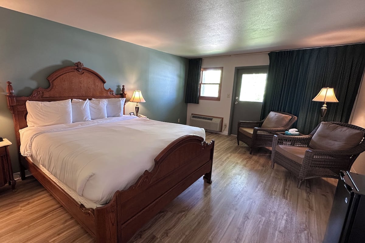 A hotel room with a wooden bed, two bedside lamps, a chair, and a desk.