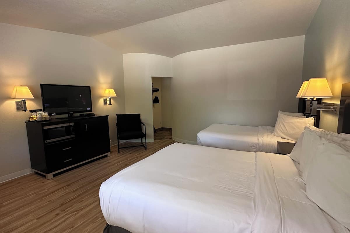 A hotel room with two beds, a TV, a desk, and two lamps.