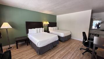 A hotel room with two beds, a desk, a chair, a lamp, and a mirror.