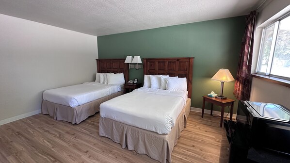 A hotel room with two single beds, a wooden headboard, a bedside table with a lamp, a telephone, and a TV on a stand. - The Shelby Inn (Shelbyville)