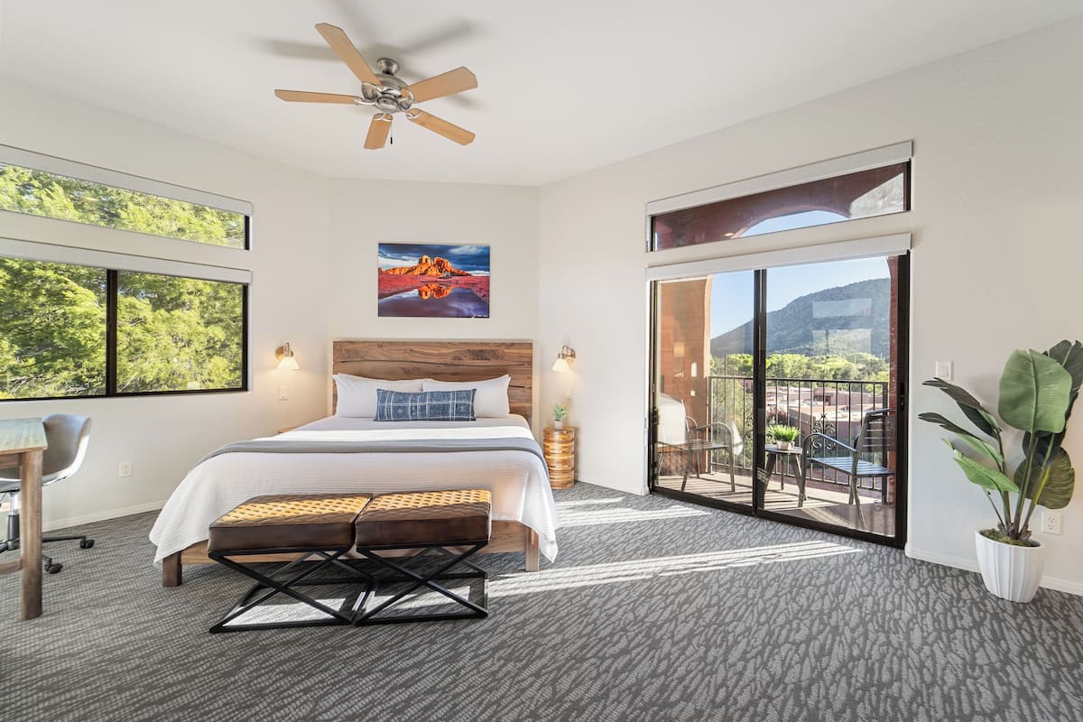 Habitación de hotel moderna con una cama grande, un escritorio, un ventilador de techo y un balcón con vistas a las montañas.