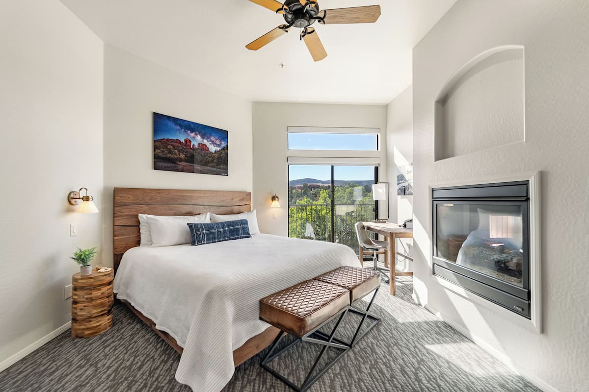 Habitación de hotel moderna con una cama grande, ventilador de techo, televisor montado y vistas al exterior.