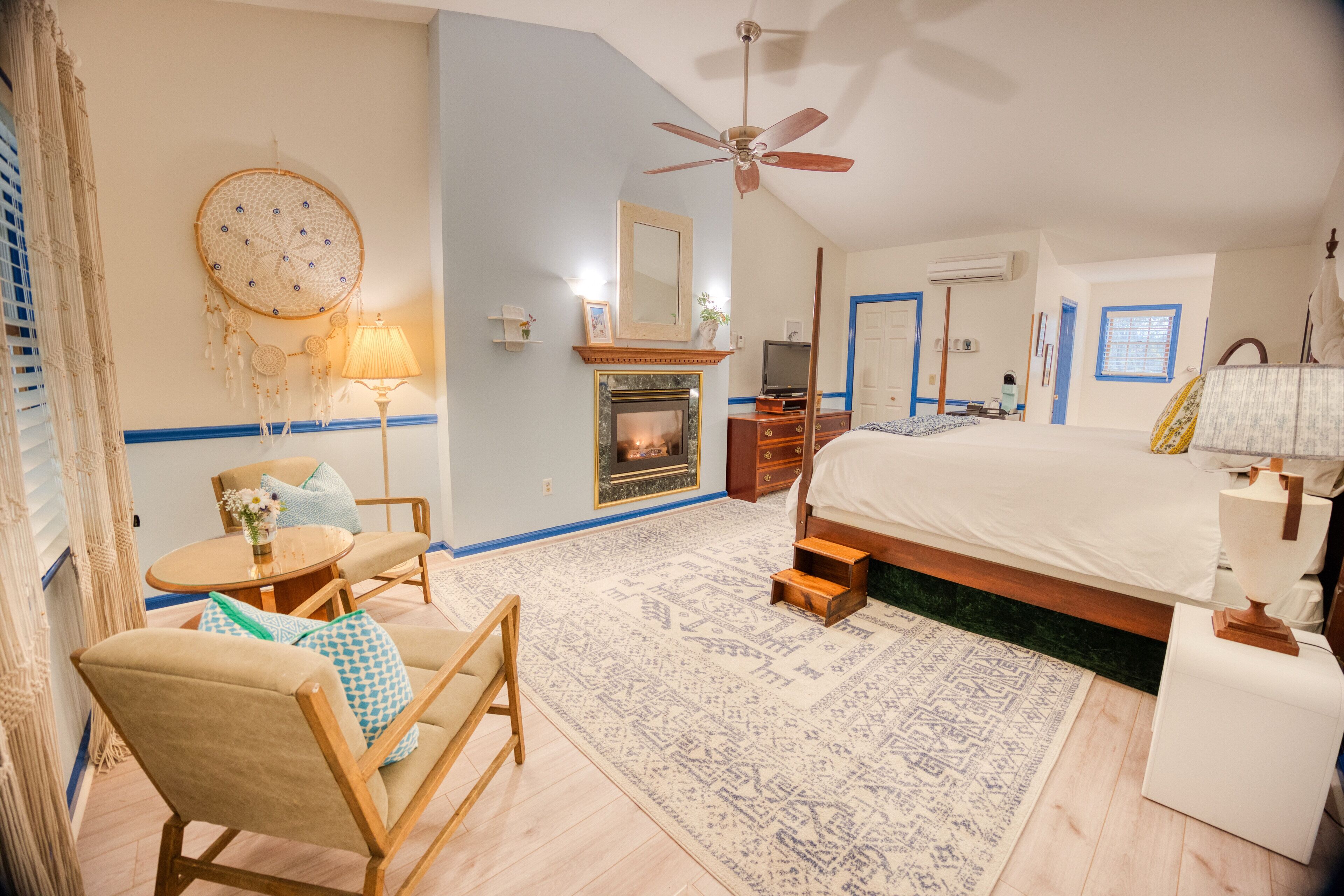 A bedroom with a bed, a ceiling fan, a fireplace, a TV, and a bedside table.
