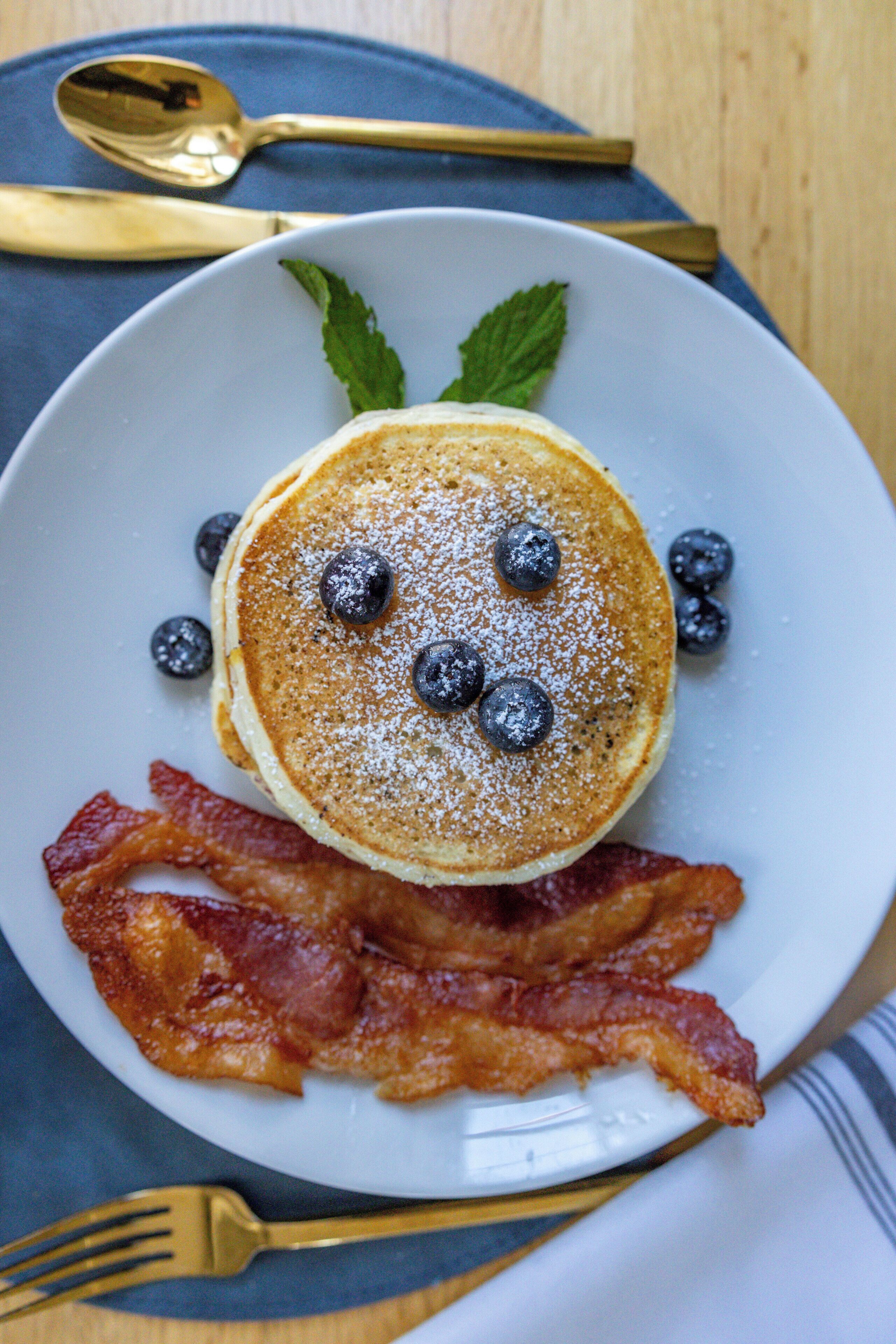 A plate with pancakes, blueberries, and bacon.