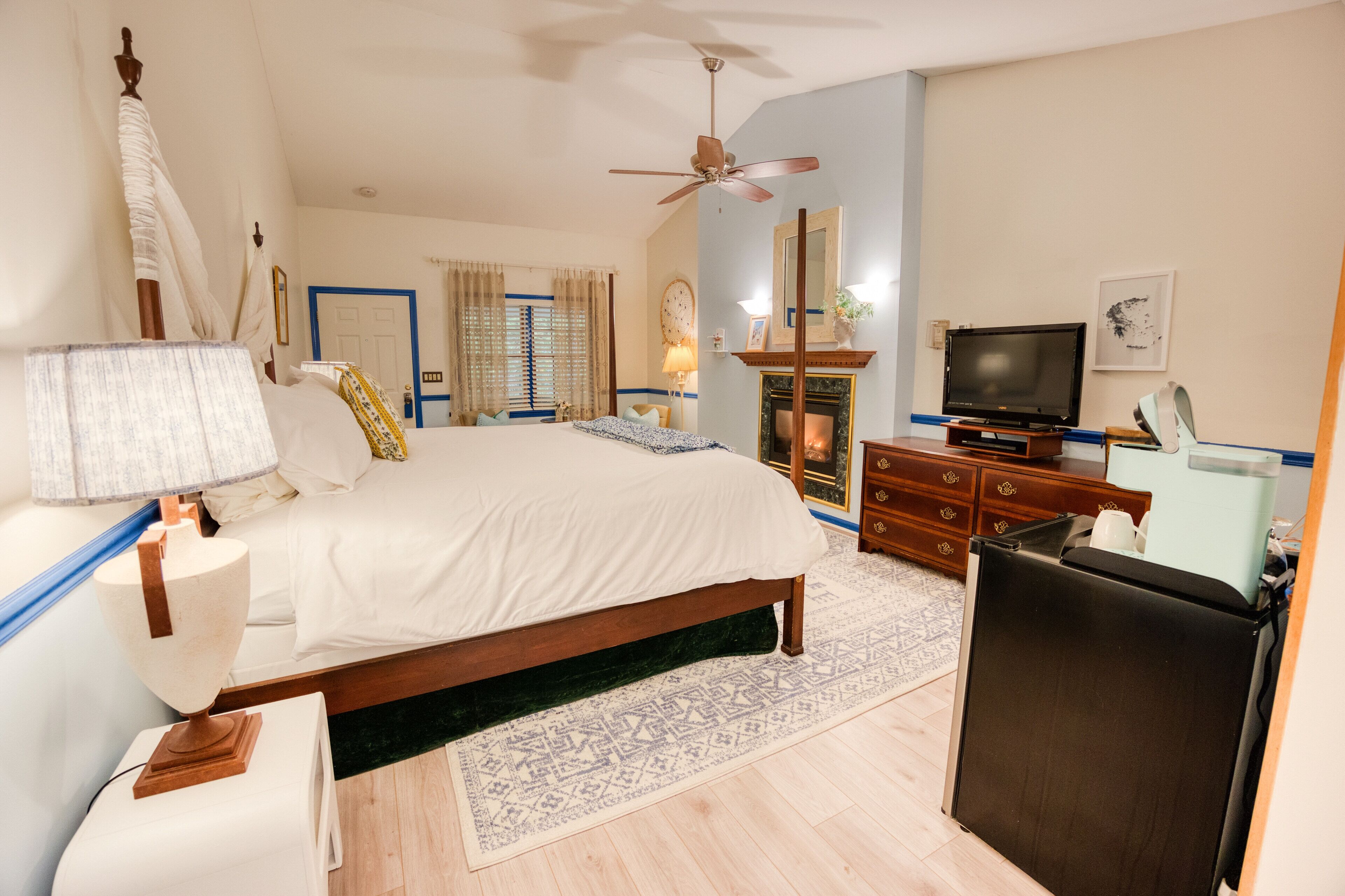 A bedroom with a bed, a television, a dresser, a mirror, and a ceiling fan.