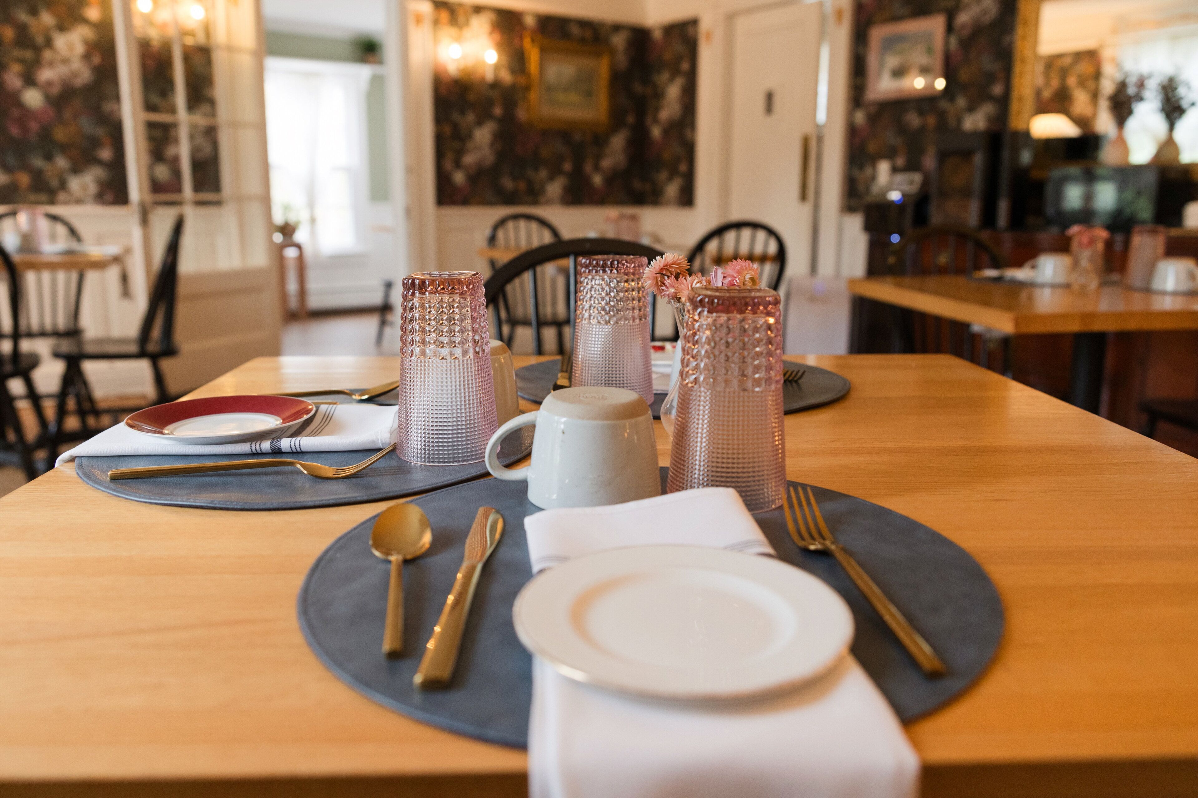 Una mesa de comedor dispuesta con platos, cubiertos y cristalería decorativa.