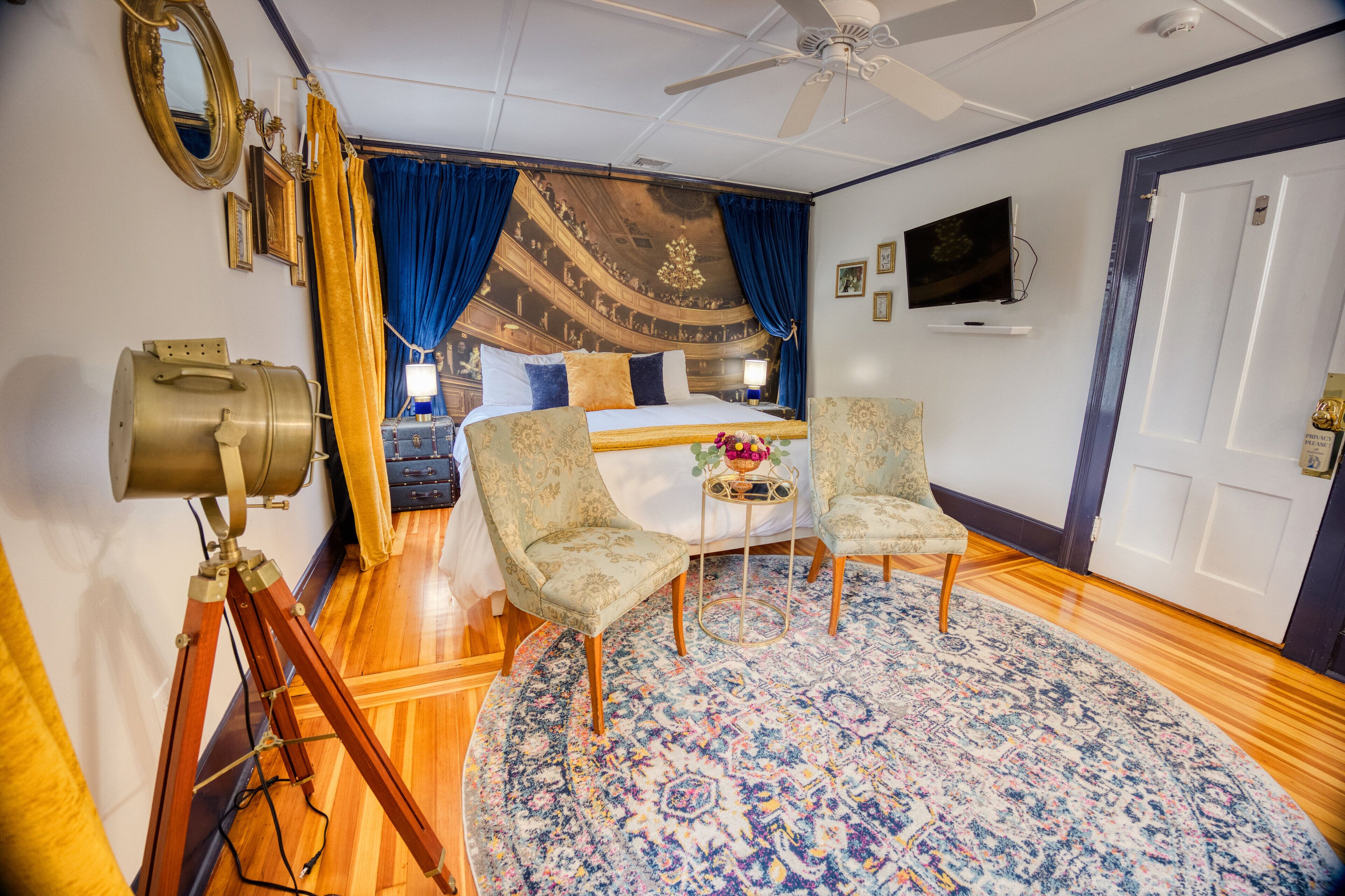 A room with a bed, two armchairs, a round rug, a ceiling fan, and a vintage telescope.