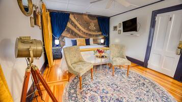 A room with a bed, two armchairs, a round rug, a ceiling fan, and a vintage telescope.