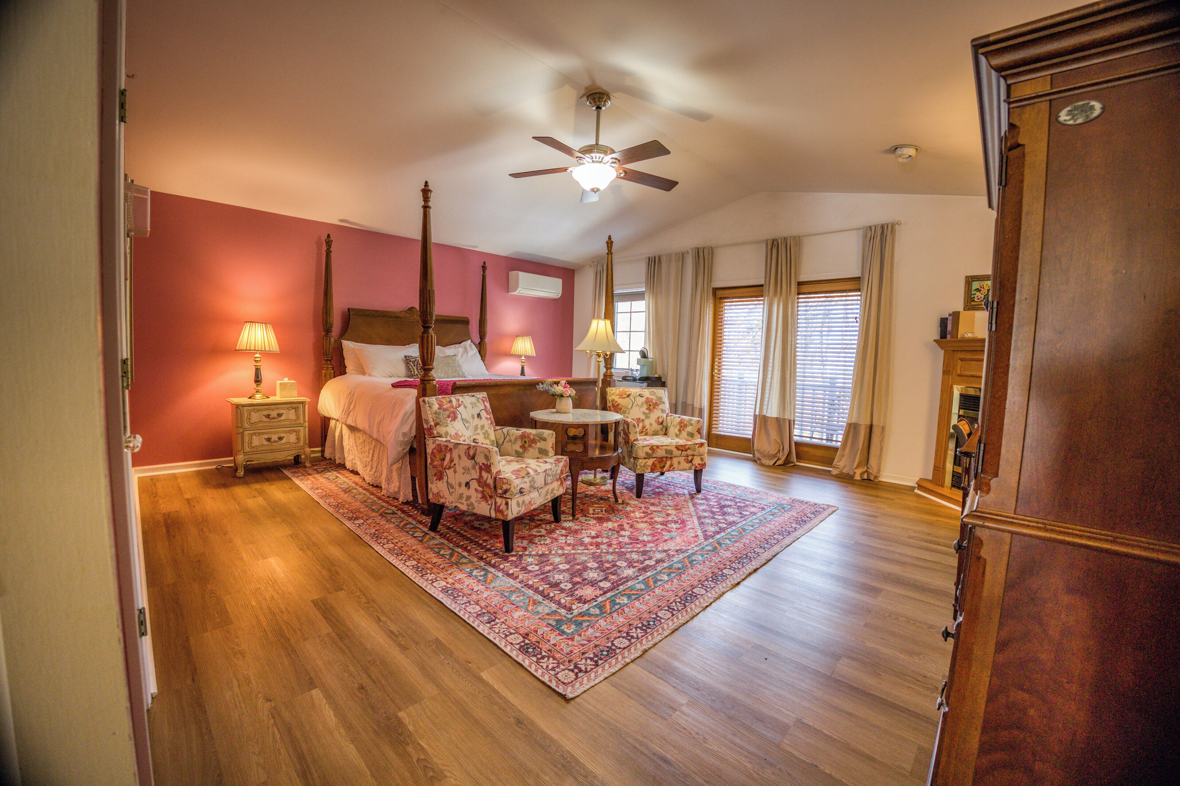 A bedroom with a four-poster bed, a ceiling fan, a wooden dresser, and a small round table with chairs.