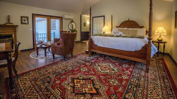 A bedroom with a four-poster bed, a large patterned rug, a chair, and a small table with a vase.