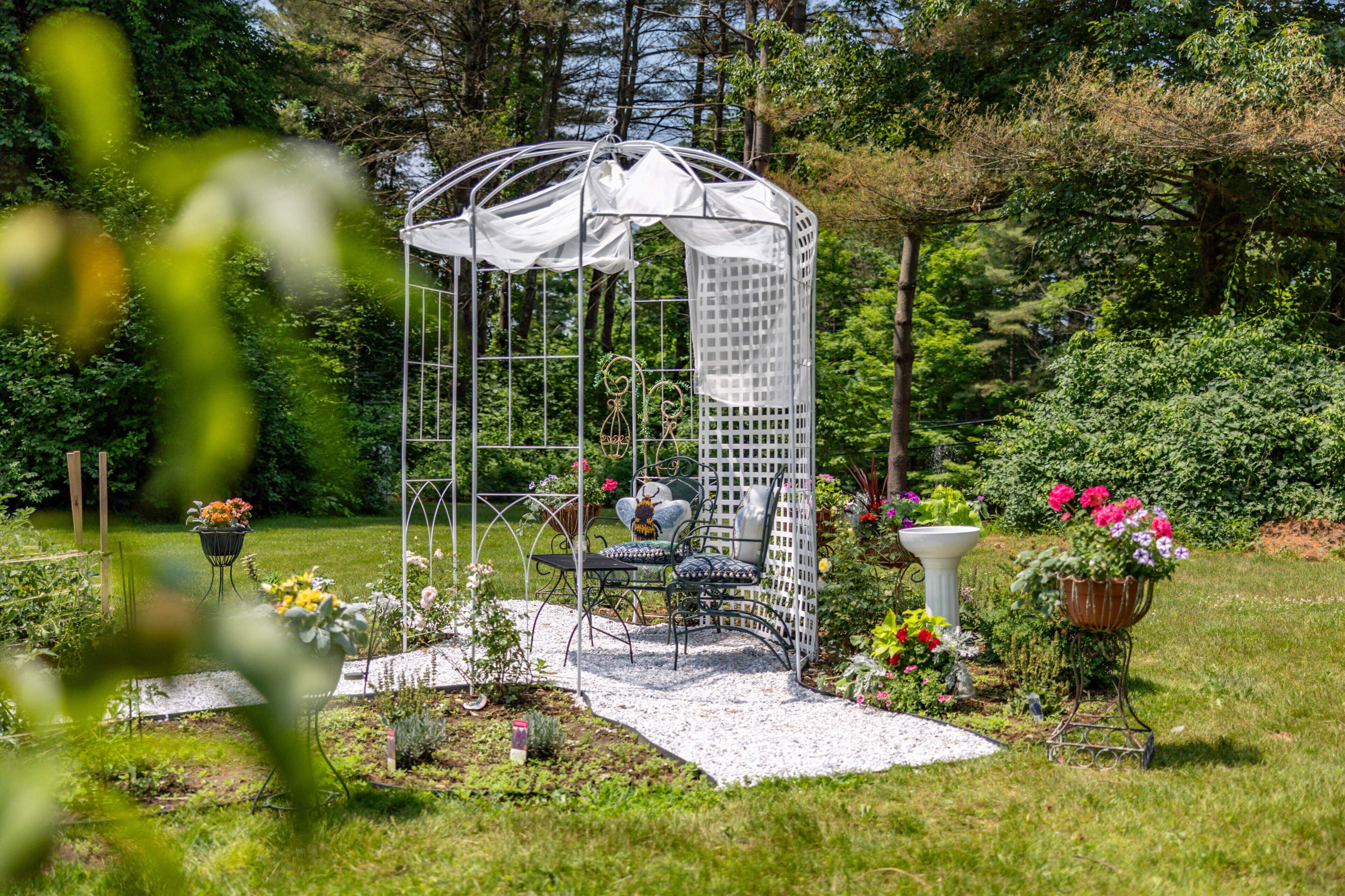 A garden with a gazebo, a table, chairs, and potted plants.