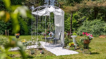 A garden with a gazebo, a table, chairs, and potted plants.