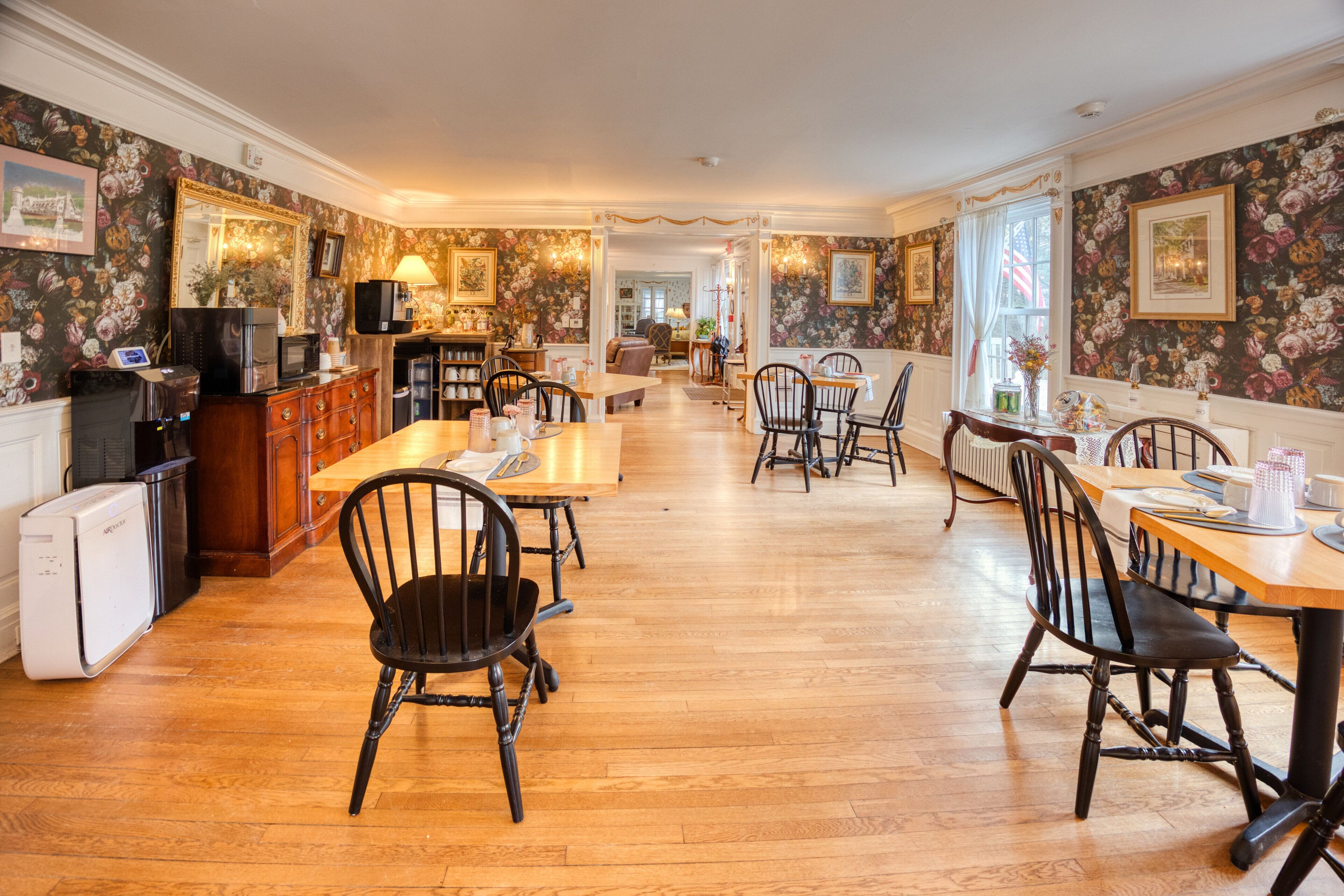 A spacious dining area with wooden flooring, black chairs, and a central table.