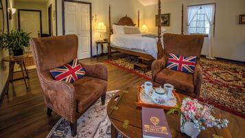 Una habitación con una cama, dos sillones con cojines con motivo de la bandera del Reino Unido, una mesa de centro con una bandeja, un libro y un jarrón de flores.